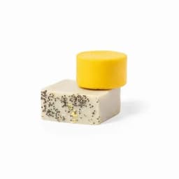 Two solid soap bars stacked, one yellow and circular on top of a rectangular bar speckled with black.