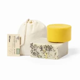 A set of solid shampoo and soap bars in yellow and creamy white, packaged with a natural fabric pouch.