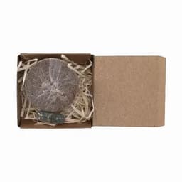 A round, grey product in a cardboard box, filled with straw-like material, featuring a small blue item.