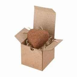 A heart-shaped product in a small open cardboard box, surrounded by shredded paper filler.