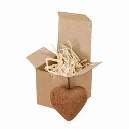 A small brown heart-shaped product beside an open cardboard box filled with straw. The box is light brown.