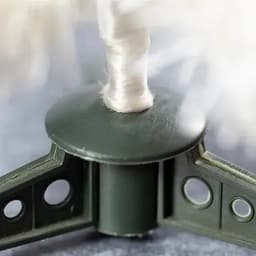 A close-up of a green product component with a white string, featuring three extending arms and a central spool mechanism.