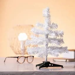 A small white, artificial Christmas tree with a black stand, placed on a table beside a pair of glasses.