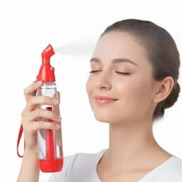 A hand sanitiser bottle in red and transparent, held by a woman with a relaxed expression and mist spraying from the nozzle.