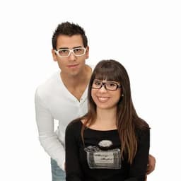 A couple poses together, both wearing glasses. The man has short dark hair and the woman has long brown hair.