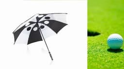 A black and white golf umbrella with a distinctive pattern, next to a golf ball on green grass.