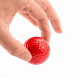 A red golf ball held between two fingers, featuring a dimpled surface for enhanced grip.