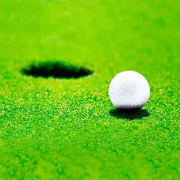 A white golf ball on green grass, near a golf hole in the background. The image features vibrant greenery.