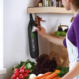 A drink bottle in a black holder with a logo, placed against a wall near fresh vegetables and herbs.