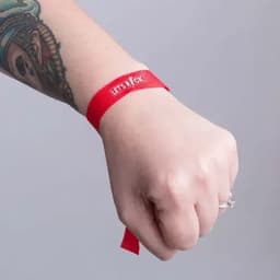 A red fabric wristband with a logo, worn on a hand with an intricate tattoo.