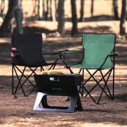 Two folding chairs, one black and one green, around a black portable fire pit in a wooded outdoor setting.