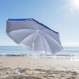 A beach umbrella with a blue trim, anchored in the sand, overlooking a sunny coastline and gentle waves.