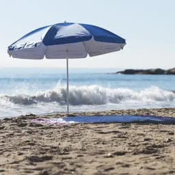 A beach umbrella featuring blue and white panels stands on sandy shores beside a gentle sea wave.