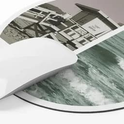 A mouse pad featuring a coastal scene with waves and a lifeguard tower in muted colours, with a smooth white edge.