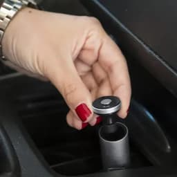 A hand gripping a silver and black device being inserted into a car's console. The setting is dark with metallic accents.
