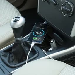 A phone charging with a visible battery percentage sits in a car's centre console next to a gear stick.