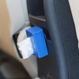 A blue container attached to a car seat, dispensing white tissues. It features a simple design with a secure fit.