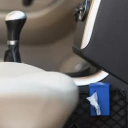 A blue car waste bin sits between the gear shift and the car seat, featuring a tissue inside.