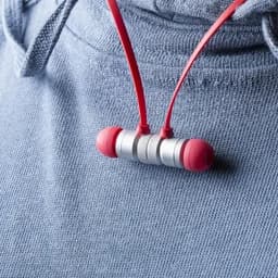Earphones with red silicone tips and a metallic connecting piece, resting on a light blue sweatshirt.