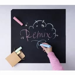 A hand writes "Remix" with colourful chalk on a blackboard, surrounded by chalk pieces and a small box.