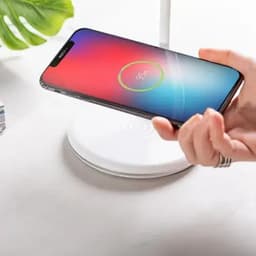 A charging pad with a sleek white base and a smartphone being placed on top, displaying a charging indicator.