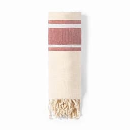 A woven towel in cream with red stripes and tassels at one end. It features a simple, textured design.