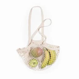 A mesh shopping bag in a light beige colour, filled with green bananas and a lime.