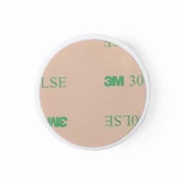 A round adhesive patch with a light beige surface and a white border, featuring discreet branding.