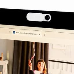 A webcam with a white cover located on a computer monitor displaying a web page. The setting includes a child playing.