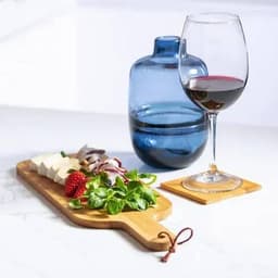 A drink bottle in blue beside a glass of red wine and a wooden platter of cheese, strawberries, and greens.
