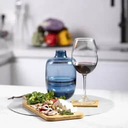 A drink bottle in blue alongside a glass of red wine and a cheese and charcuterie platter on a wooden board.