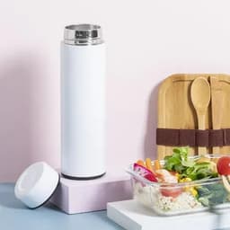 A drink bottle in white with a silver lid, placed next to a salad and wooden utensils on a pink background.
