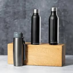 A drink bottle collection featuring three metal bottles in black and grey, presented on a wooden block.
