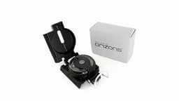 A black compass in a folded position, with a grey box visible in the background. The compass includes a branding logo.