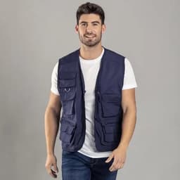 A man wearing a navy blue multi-pocket vest over a white t-shirt, standing against a grey background.