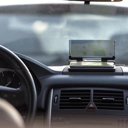 A dashboard mount with a smartphone displaying a map. The setting is inside a car, with the steering wheel visible.