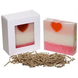 A soap box with a clear window, featuring a layered pink and white soap with a heart shape on top, surrounded by shredded paper.