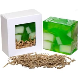 A green soap bar with white accents, packaged in a white box with a window, surrounded by tan paper shreds.