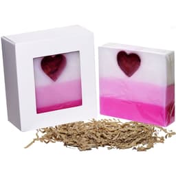 A pink and white soap with a heart shape inside, presented in a square white box, surrounded by shredded paper.