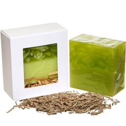 A green soap bar in a box with a window, accompanied by shredded brown packaging material. The box has a logo.