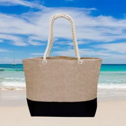 A large bag with a beige upper section and a black lower section, featuring rope handles against a beach backdrop.