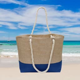 A large beach bag in beige and navy blue, featuring rope handles, set against a coastal background.