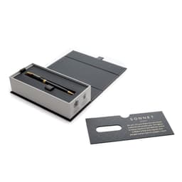 A black and gold ballpoint pen sits in a grey box, accompanied by a rectangular card with a logo.
