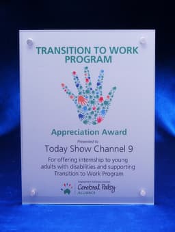 A clear acrylic award plaque with a floral handprint design and a blue satin background. It features a logo at the top.