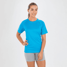 A woman is wearing a bright blue Adult Impact Performance Aircool T-Shirt paired with grey shorts, smiling at the camera.