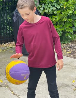 A burgundy longsleeve shirt worn by a child playing with a purple and yellow basketball outdoors.