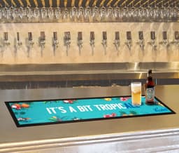 A bar runner in vibrant teal featuring tropical designs, placed on a polished bar with drinks nearby.