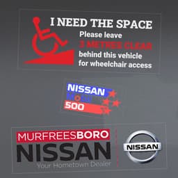 Assorted vinyl stickers featuring a wheelchair access symbol, a racing logo, and a car dealership logo with silver details.