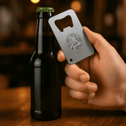 A drink bottle opener resembling a credit card, made of stainless steel, held in a hand next to a dark bottle.