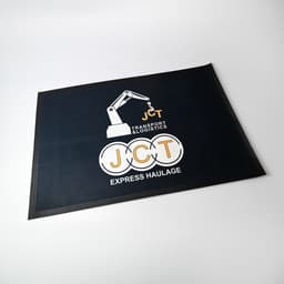 A promotional mat featuring a black background with yellow and white graphics, including a crane and 'JCT' branding.